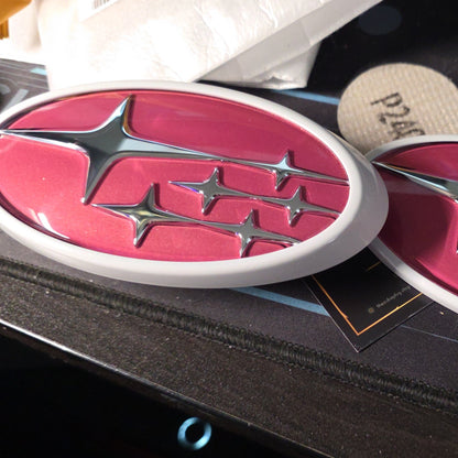 Close-up of a pink and silver car emblem on a black surface.